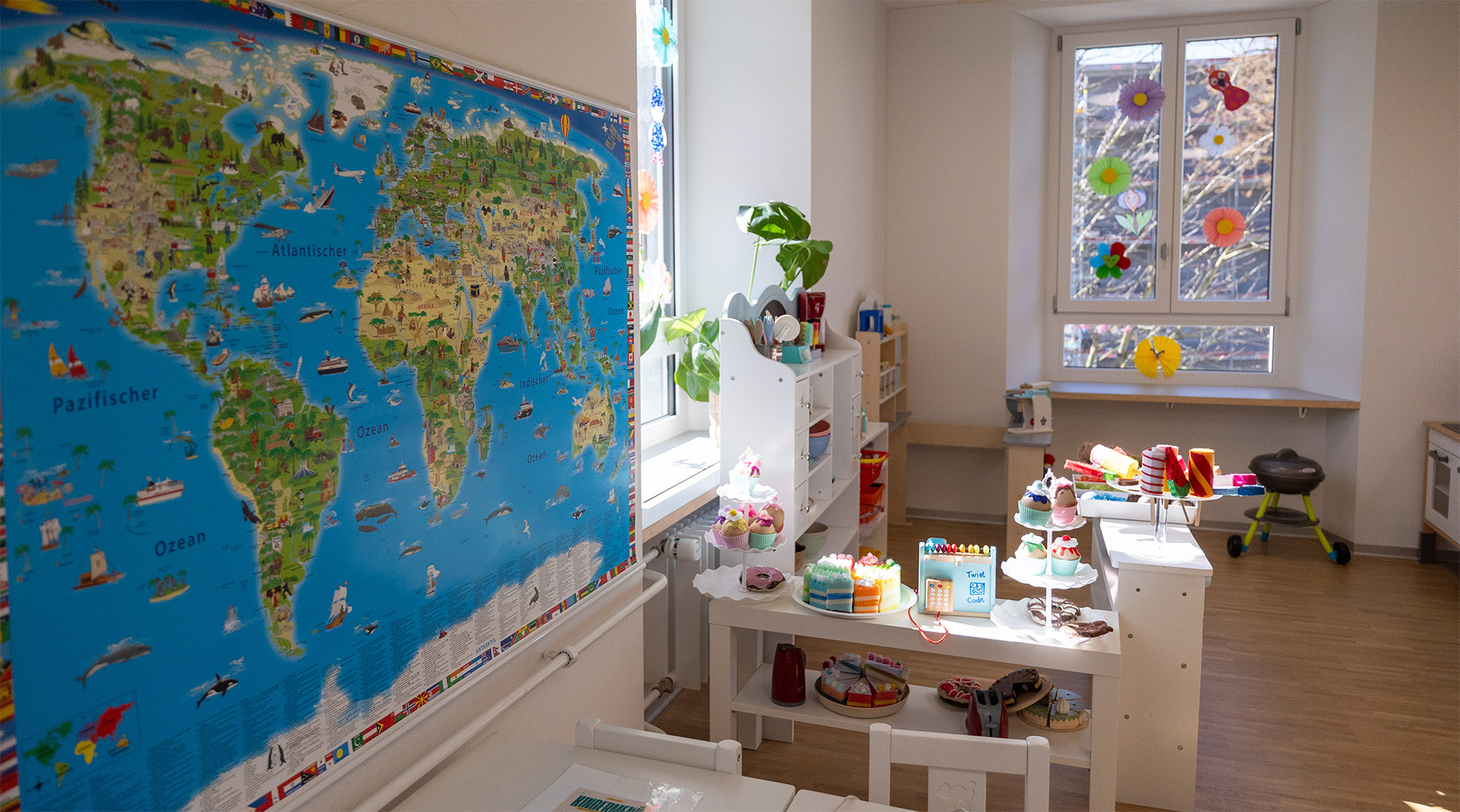Kindgerecht eingerichteter Spielbereich der Tagesstrukturen Wohlen Halde mit Weltkarte, Spielküche, Verkaufsladen und Rollenspielmaterial.
