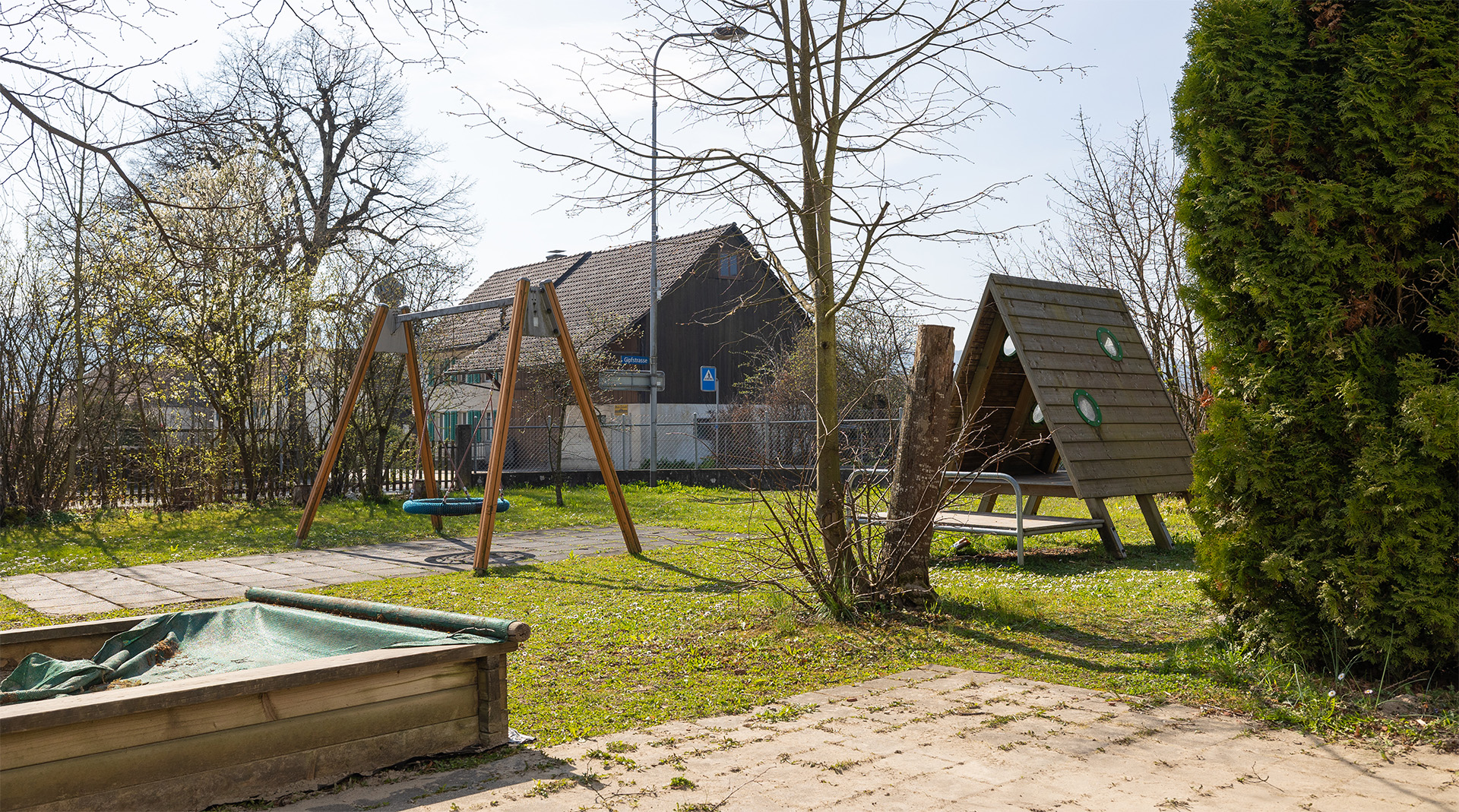 Aussenbereich der Tagesstrukturen Würenlos mit Schaukel, Sandkasten und Spielmöglichkeiten im Grünen.
