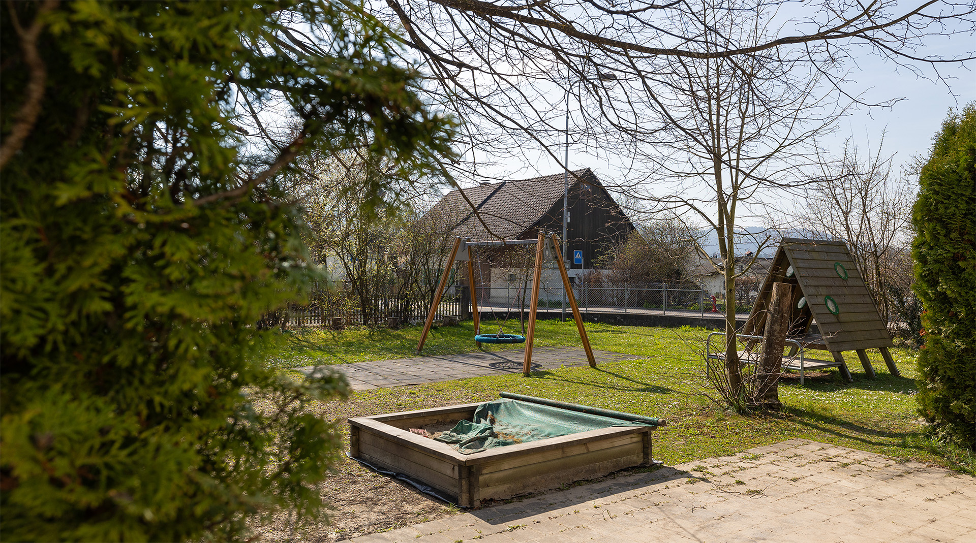 Spielgarten der Tagesstrukturen Würenlos mit Sandkasten, Schaukel und naturnahem Aussenbereich.