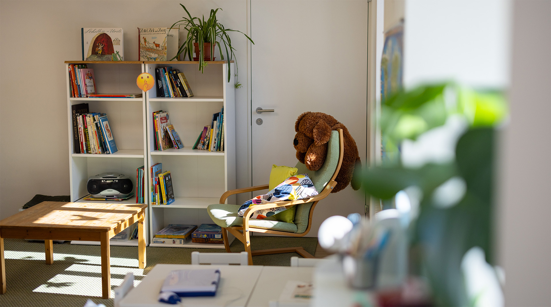 Gemütliche Lese- und Ruheecke der Tagesstrukturen Wohlen Halde mit Bücherregal, Sessel, kleinem Tisch und heller Fensterfront.