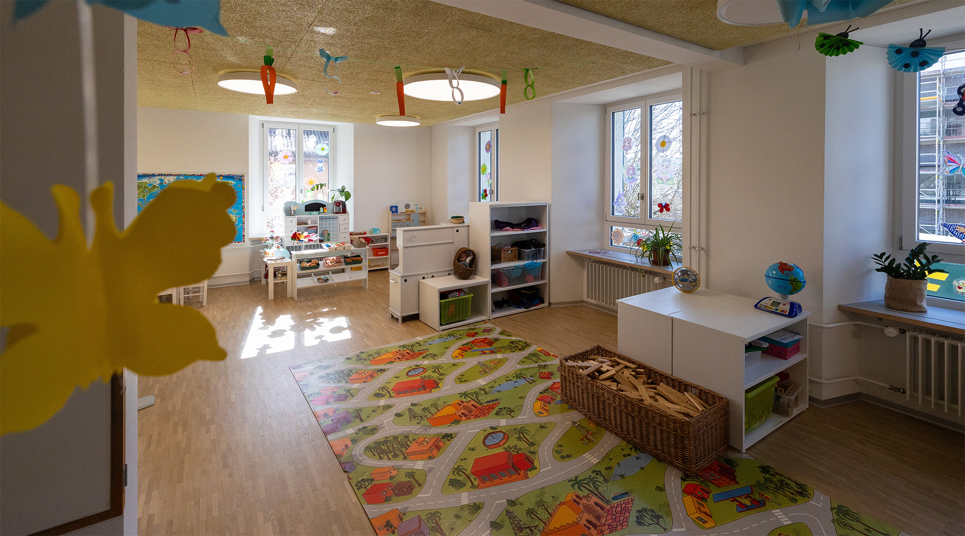 Einladender Spielraum der Tagesstrukturen Wohlen Halde mit Teppich, Spielmöbeln, Kinderküche und viel Platz zum freien Spielen.